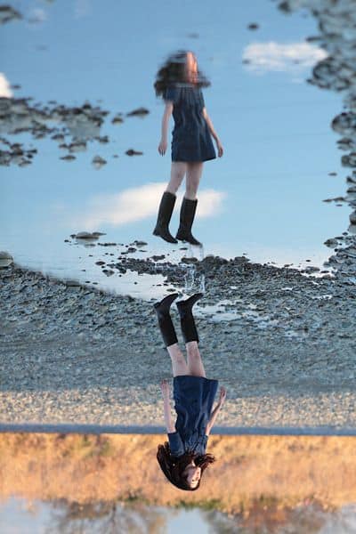 pretty japanese girl floats above her reflection in a puddle