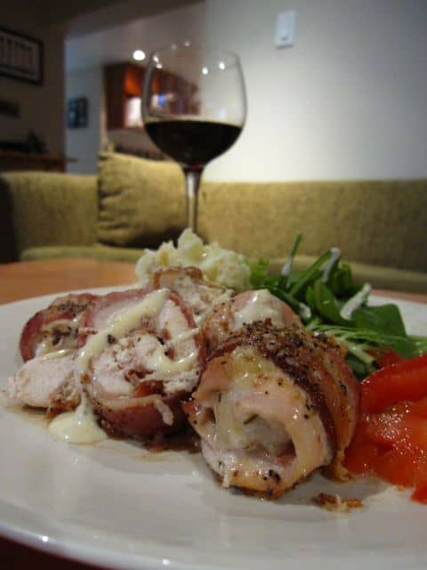 A Glass Of Wine On A Table With Bacon Wrapped Chicken