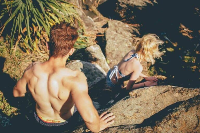 topless man behind woman walking on gray rock formation during daytime