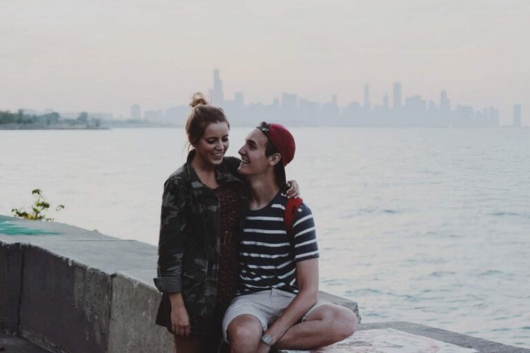 young couple sitting on ledge embracing and smiling happy