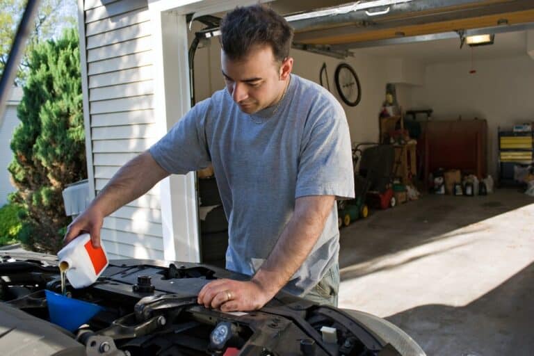 man adding oil to their car outside their garage