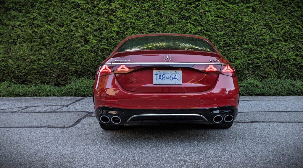 Luxury red Mercedes-Benz E-Class AMG sports sedan parked outdoors with lush green bushes in the background.
