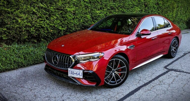 Red Mercedes-Benz luxury sedan parked on a paved driveway with green hedge background, emphasizing performance and style.