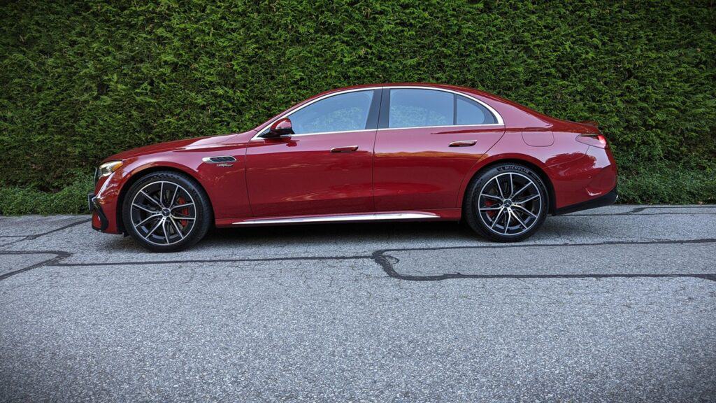 Luxurious red sedan parked on asphalt road with green hedge backdrop, highlighting sleek design and high-performance features.
