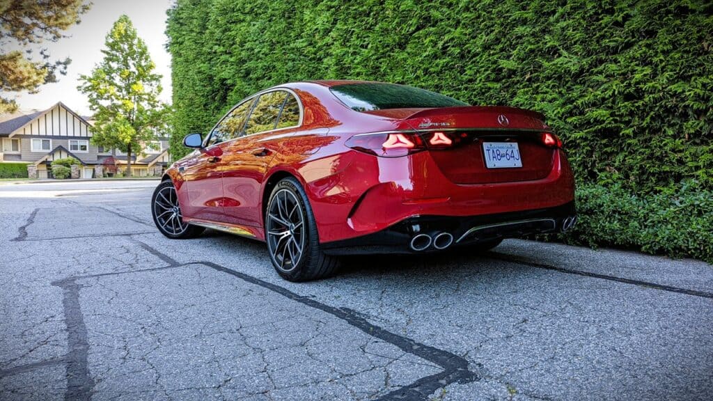 Red Mercedes-Benz luxury sedan parked on suburban street with greenery and houses in background.