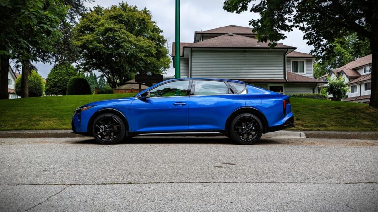 Blue sports car parked on residential street with green trees and houses in the background, showcasing modern automotive design and urban lifestyle.
