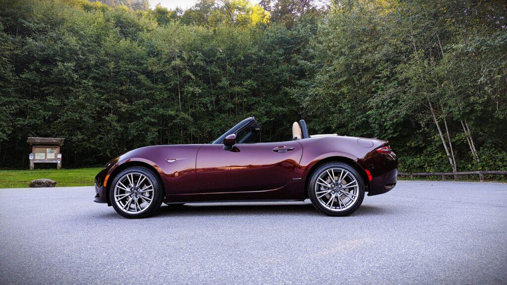 Luxurious maroon convertible sports car parked on a scenic road with a forest background.
