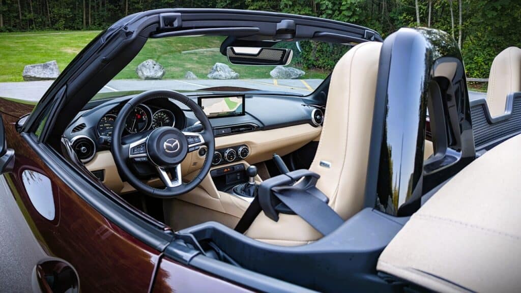 Luxury Mazda convertible interior with beige leather seats and advanced dashboard features, parked on a scenic green area.