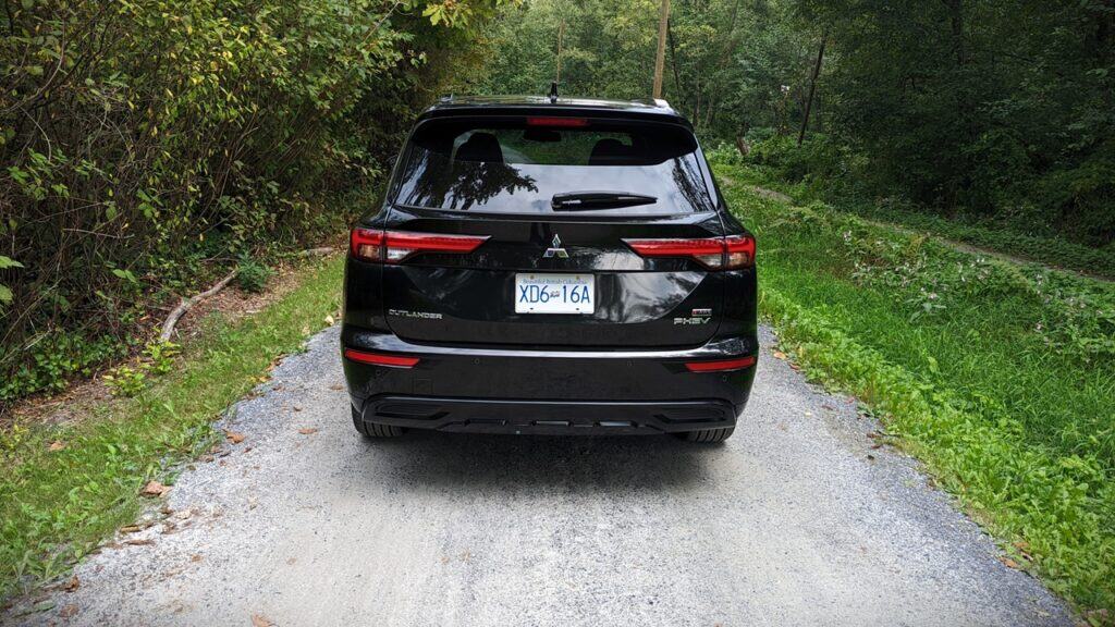 2025 Mitsubishi Outlander PHEV Noir Review 9 Black Mitsubishi Outlander SUV parked on a gravel path in a lush green forest setting.