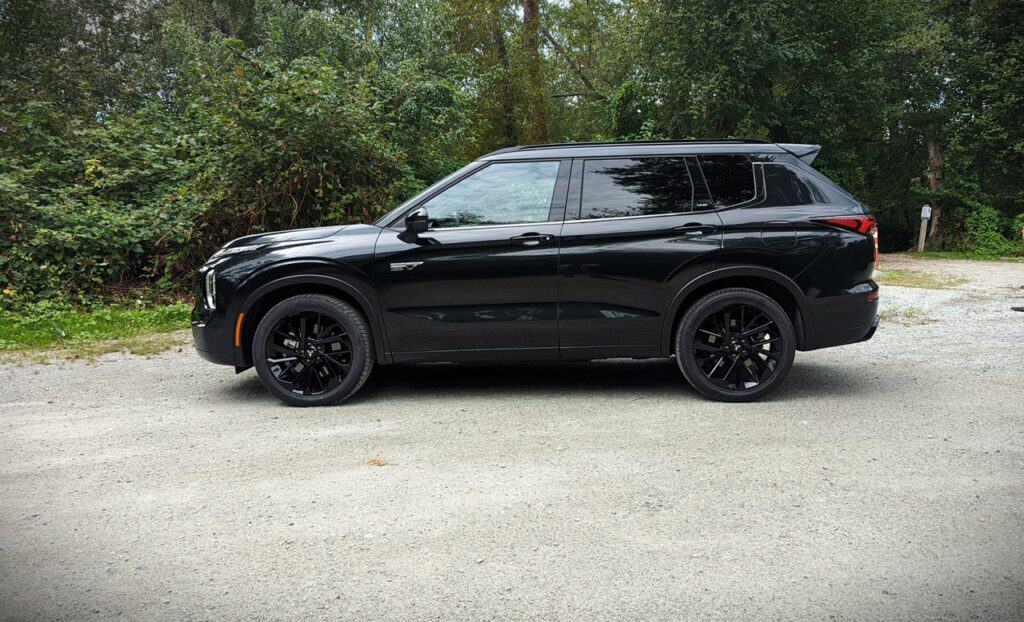 2025 Mitsubishi Outlander PHEV Noir Review 7 Black SUV parked on a gravel path surrounded by green foliage, showcasing modern automotive design and luxury vehicle features.