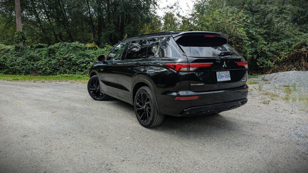 2025 Mitsubishi Outlander PHEV Noir Review 8 Sleek black Mitsubishi Outlander SUV parked on gravel driveway surrounded by lush green trees, showcasing modern design and outdoor adventure readiness.
