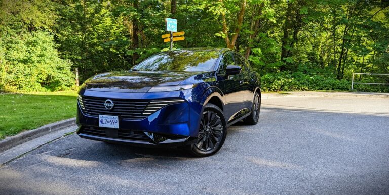 Sleek blue Nissan electric vehicle parked on a scenic road with lush green trees in the background.