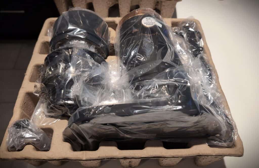 Black electronic accessories and gadgets in plastic wrapping, packaged in foam tray for safe shipping or storage, on a neutral background.