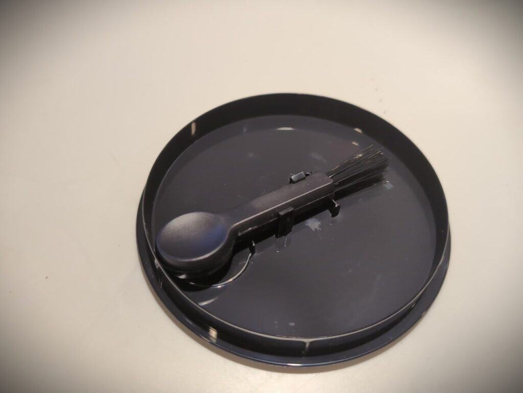 Black spray bottle with a nozzle on a round black tray, used for cleaning or disinfecting, on a plain surface.