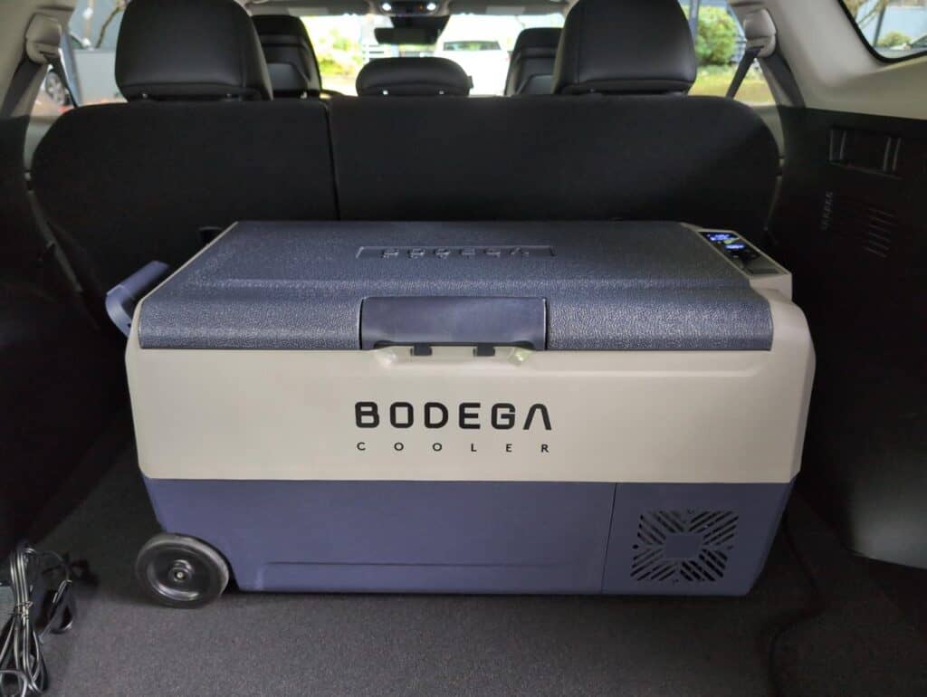 A dual-zone cooler in an SUV trunk surrounded by camping gear. High-quality portable Bodega cooler in the trunk of a vehicle for outdoor adventures, camping, or road trips, featuring efficient cooling and spacious design.
