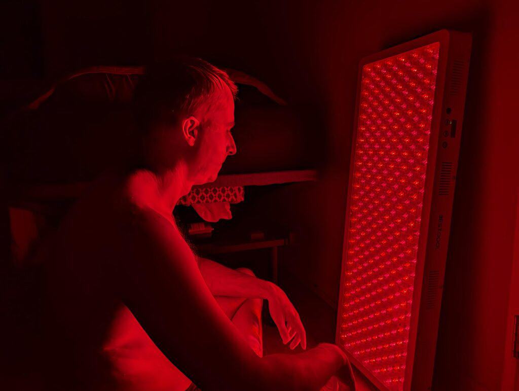 BestQool Red Light Therapy Pro300 Review: 9 Bright Benefits 9 Red LED light therapy device illuminating a person’s face in a dark room, promoting skin rejuvenation and relaxation. Ideal for skincare routines, anti-aging treatments, and health wellness.