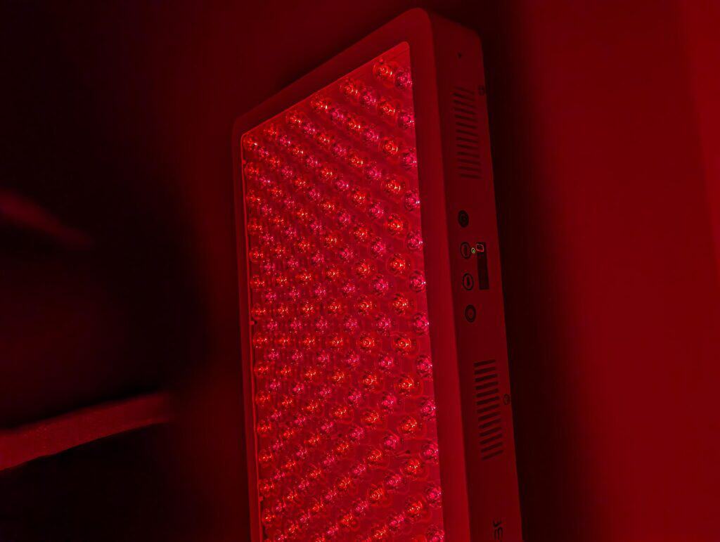 BestQool Red Light Therapy Pro300 Review: 9 Bright Benefits 10 Red LED light therapy device with multiple bulbs for skincare, pain relief, or therapeutic treatments, glowing in a dark environment.
