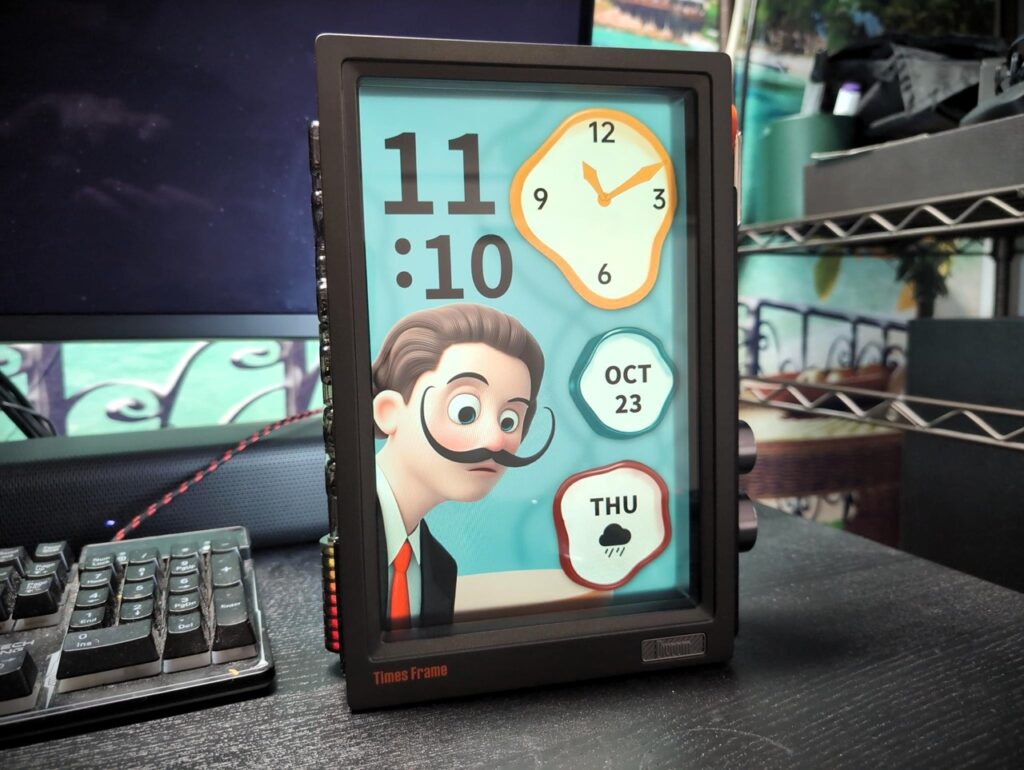 Divoom Times Frame Review 3 Colorful digital clock displaying the time, date, weather, and a cartoon character with a mustache on a black desk.