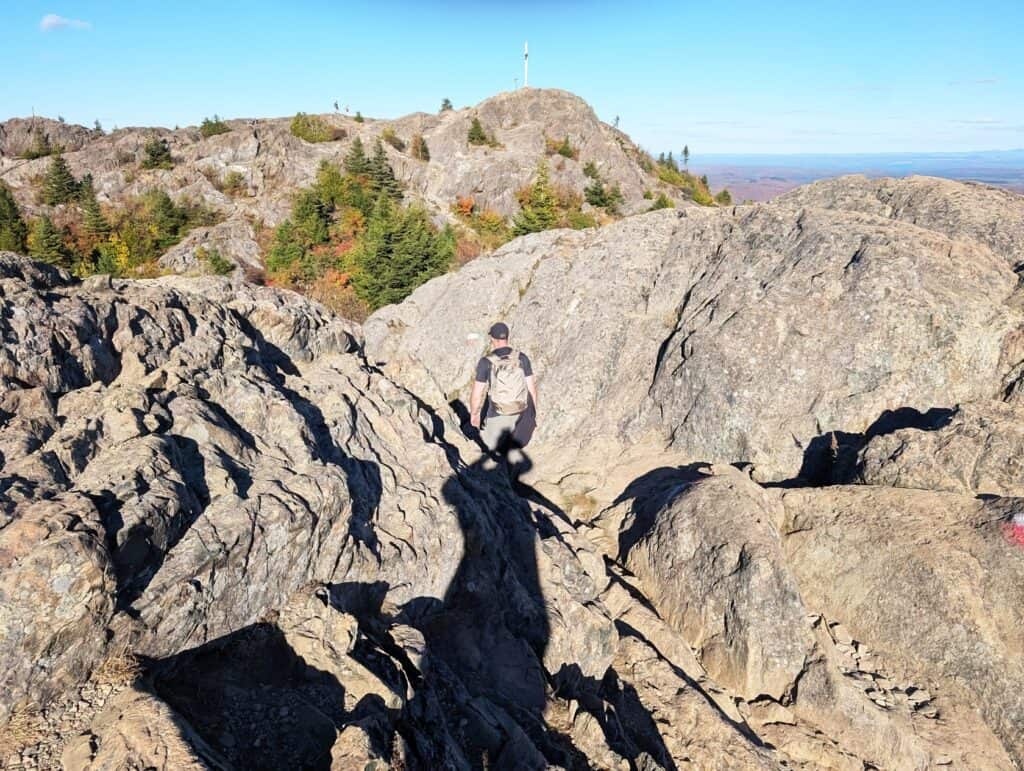 Eberlestock Apprentice Backpack Review: Worth It in 2025? 8 A hiker in a black cap and backpack ascending a rocky mountain trail during daytime with clear skies.
