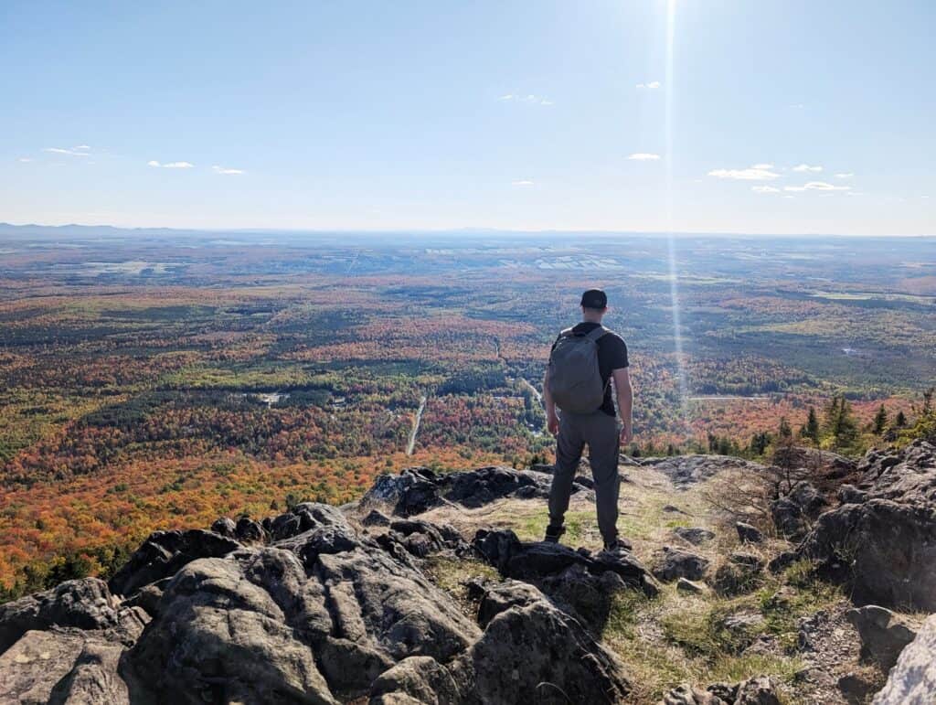 Eberlestock Apprentice Backpack Review: Worth It in 2025? 9 A man with a backpack stands on a mountain cliff overlooking a vast forested landscape during daytime, enjoying the scenic view and fresh air.