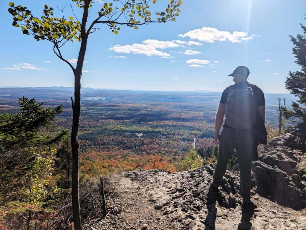 Eberlestock Apprentice Backpack Review: Worth It in 2025? 7 A hiker enjoying a scenic view from a mountain overlook with a vast forest and clear sky in the background.