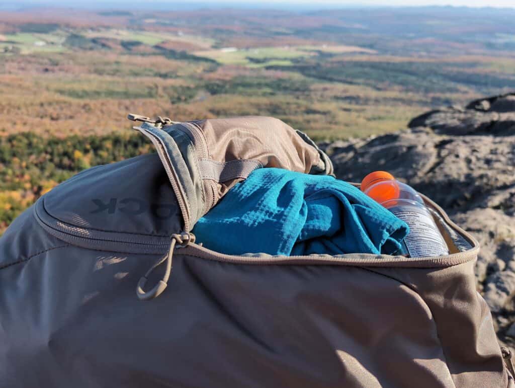 Eberlestock Apprentice Backpack Review: Worth It in 2025? 6 Backpack with water bottle and blue towel on a mountain summit overlooking a scenic valley during daytime.