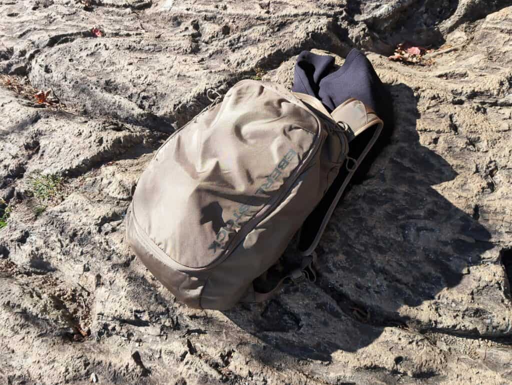 Eberlestock Apprentice Backpack Review: Worth It in 2025? 2 Beige backpack and black hoodie on rocky terrain, outdoor adventure gear, travel essentials on rugged natural surface.