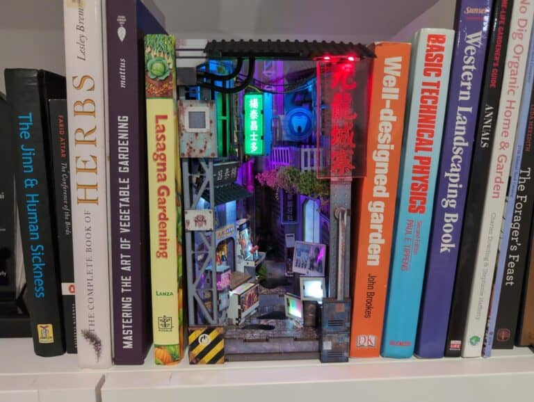 Neon-lit miniature Asian street scene model with bookshelves in the background.