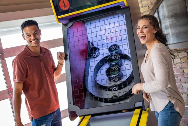 Bright enthusiastic young adults playing air hockey at an arcade, smiling and enjoying fun recreational activities, showcasing entertainment, friendship, and leisure moments.