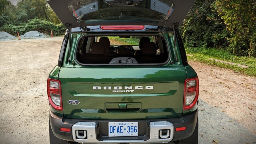 2025 Ford Bronco Sport Outer Banks Review 9 Off-road green Ford Bronco Sport SUV with open rear hatch, parked on gravel trail surrounded by trees and nature.