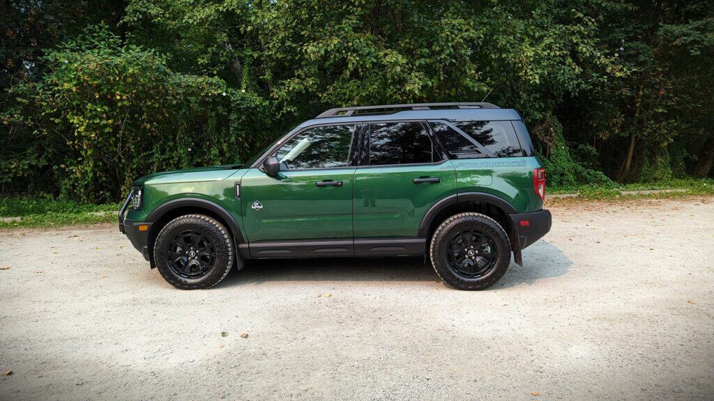 2025 Ford Bronco Sport Outer Banks Review 6 Green off-road SUV parked on gravel road with lush greenery in the background, showcasing rugged vehicle design and outdoor adventure readiness.