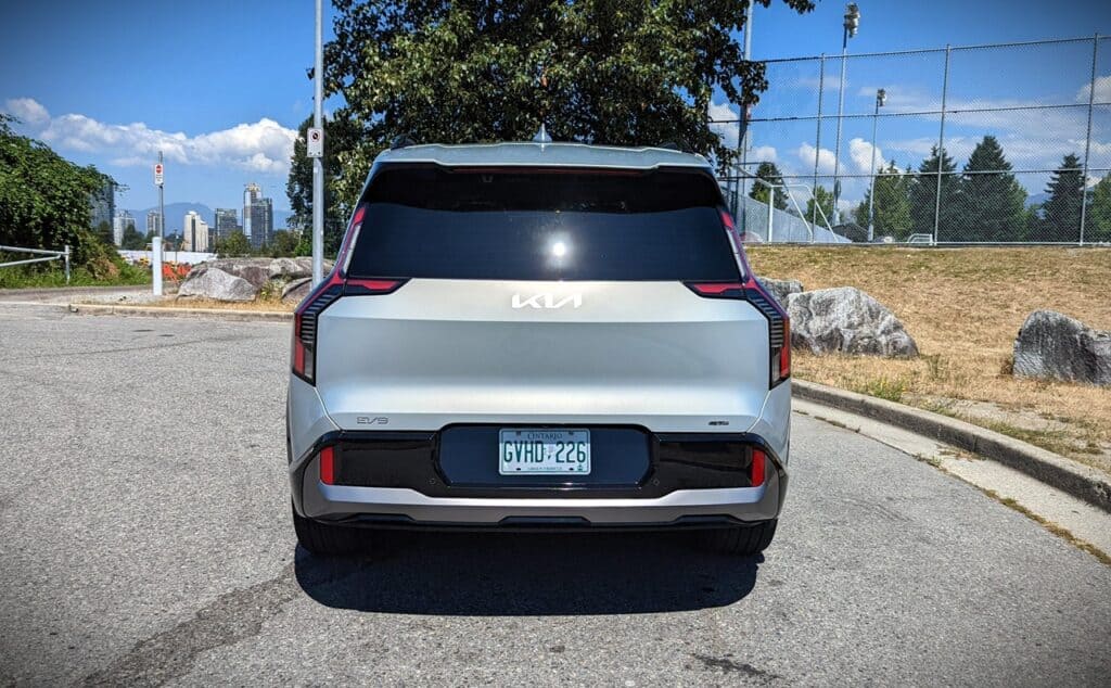 2025 Kia EV9 GT-Line Review 10 1. Modern silver Kia SUV parked on urban street with city skyline and park background, showcasing contemporary vehicle design.