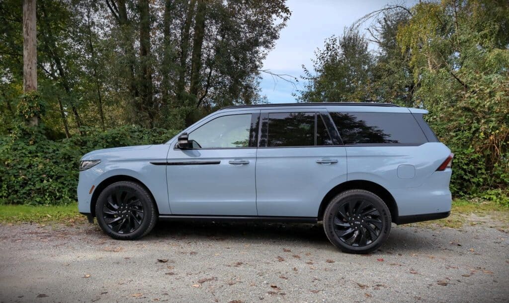 2025 Lincoln Navigator Reserve Review 6 2025 Lincoln Navigator SUV parked on a gravel path with a backdrop of trees and greenery, showcasing modern design, black wheels, and sleek exterior, perfect for eco-conscious urban driving.