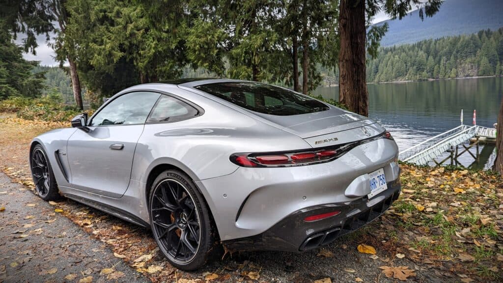 2025 Mercedes-AMG GT 63 4MATIC+ Coupe Review 11 Sleek silver Mercedes-AMG sports car parked near a serene lakeside surrounded by tall trees and mountain scenery.