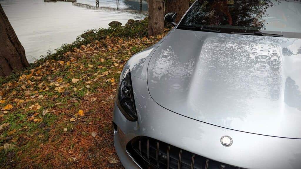 2025 Mercedes-AMG GT 63 4MATIC+ Coupe Review 13 Sleek silver sports car parked near a lake with autumn leaves on the ground and trees reflected on the hood, showcasing luxury vehicle aesthetics and scenic nature backdrop.