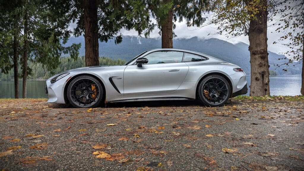 2025 Mercedes-AMG GT 63 4MATIC+ Coupe Review 5 Luxurious silver sports car parked by a lake amidst trees with mountain views in the background.