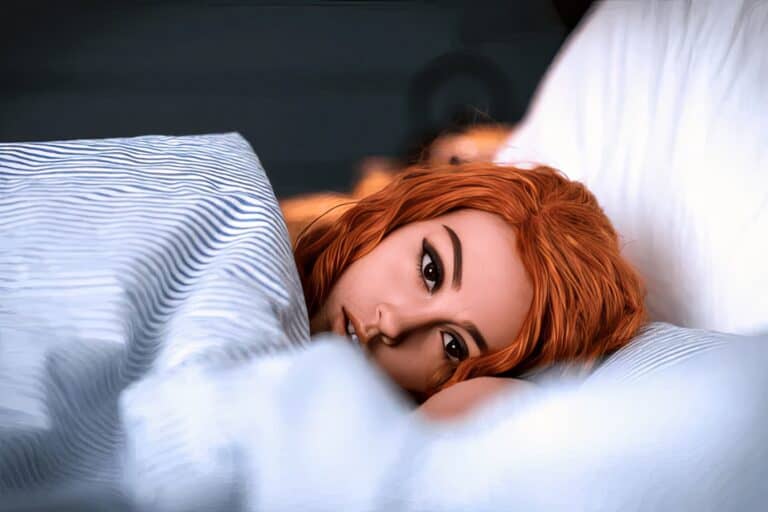 Beautiful woman with red hair lying in bed, relaxing on pillow, attractive model with flawless skin and expressive eyes, cozy bedroom scene perfect for lifestyle and beauty blog imagery.