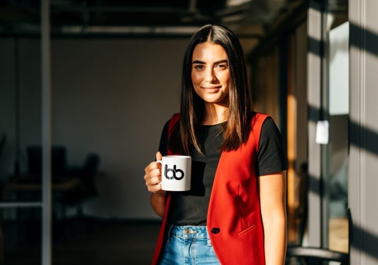 Confident young woman smiling with coffee mug in bright office space.