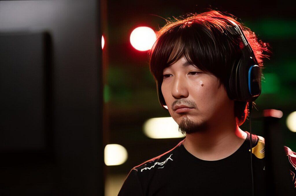 Daigo Umehara: The Legendary Beast's Complete Fighting Game Journey 4 Focuses on a young man with long dark hair, wearing gaming headphones, intensely gaming at a computer station in a vibrant, nightlife-inspired environment.