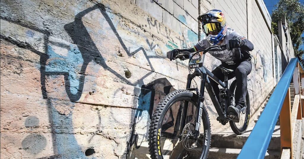 A man in his mid-30s casually rides a mountain bike down a steep street in Valparaíso. High-performance mountain biker riding up outdoor stone stairs on a rugged urban trail.