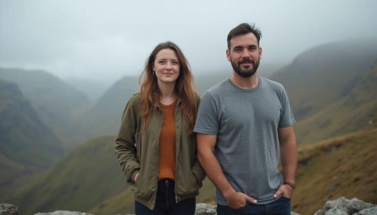 Two young adults, a woman and a man, standing outdoors on a mountain landscape with misty hills in the background, dressed casually, enjoying nature and adventure.