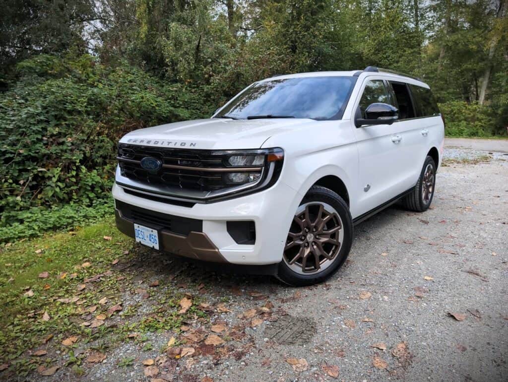 2025 Ford Expedition King Ranch Review 8 High-resolution image of a white Ford Expedition parked on a gravel path surrounded by lush greenery, showcasing its modern design, black accents, and rugged build. Perfect for outdoor adventures and family trips, this vehicle combines style with practicality. The image highlights the SUV’s bold front grille, sleek body lines, and off-road capabilities, making it ideal for exploration and outdoor lifestyles.