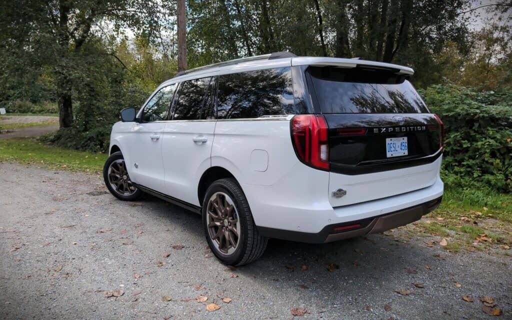 2025 Ford Expedition King Ranch Review 10 A white Ford Expedition SUV parked on a gravel roadside, surrounded by green trees and fall foliage, showcasing rugged outdoor capabilities and stylish design.