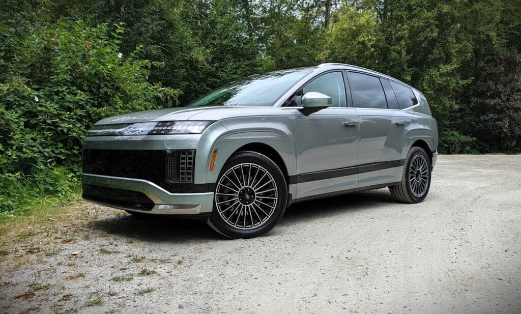 2026 Hyundai Ioniq 9 Preferred Ultimate Calligraphy Review 7 An image of a sleek, modern electric SUV with a futuristic design parked on a gravel path surrounded by greenery, highlighting advanced automotive technology and eco-friendly transportation options.