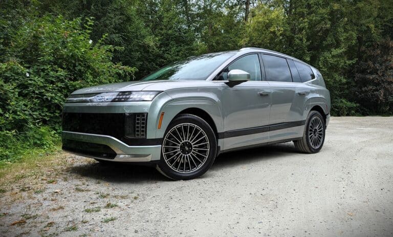 An image of a sleek, modern electric SUV with a futuristic design parked on a gravel path surrounded by greenery, highlighting advanced automotive technology and eco-friendly transportation options.