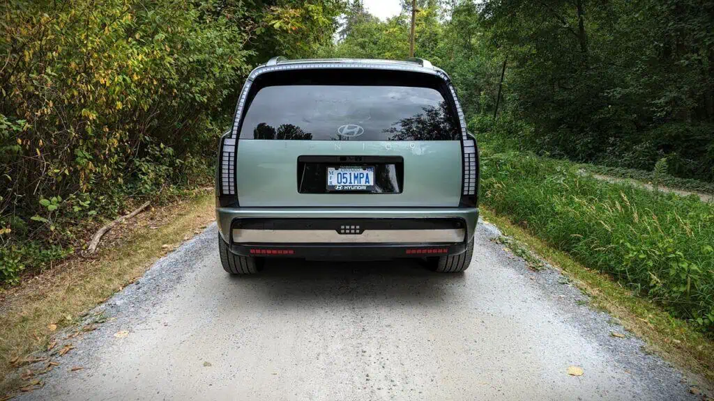 2026 Hyundai Ioniq 9 Preferred Ultimate Calligraphy Review 10 An innovative Hyundai CONCEPT vehicle parked on a gravel road surrounded by lush green trees and bushes, showcasing modern automotive design with a sleek, matte finish and advanced taillight features.