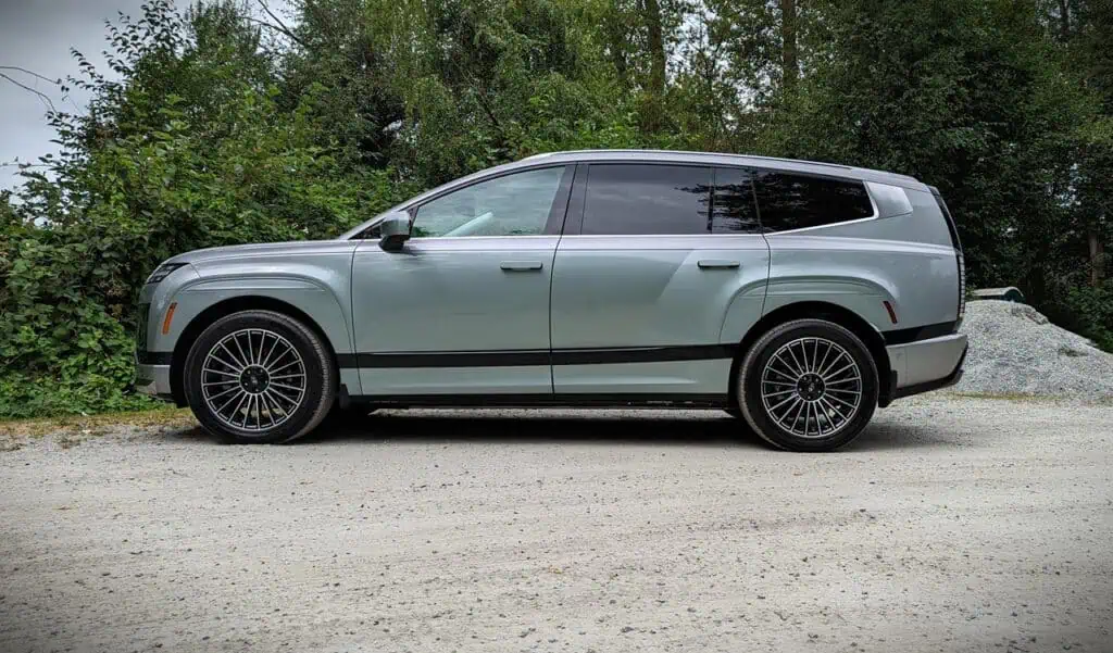 2026 Hyundai Ioniq 9 Preferred Ultimate Calligraphy Review 8 High-quality image of a sleek, modern luxury SUV parked on a gravel surface surrounded by lush greenery, perfect for car enthusiasts and those interested in upscale vehicles.