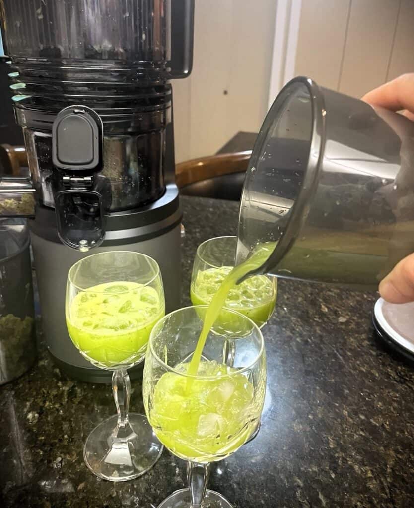 Bright green juice being poured into glasses with ice, fresh and healthy beverage, kitchen setting, homemade juice, wellness drink, antioxidant-rich, nutritious, vibrant color, detox drink, lifestyle update.
