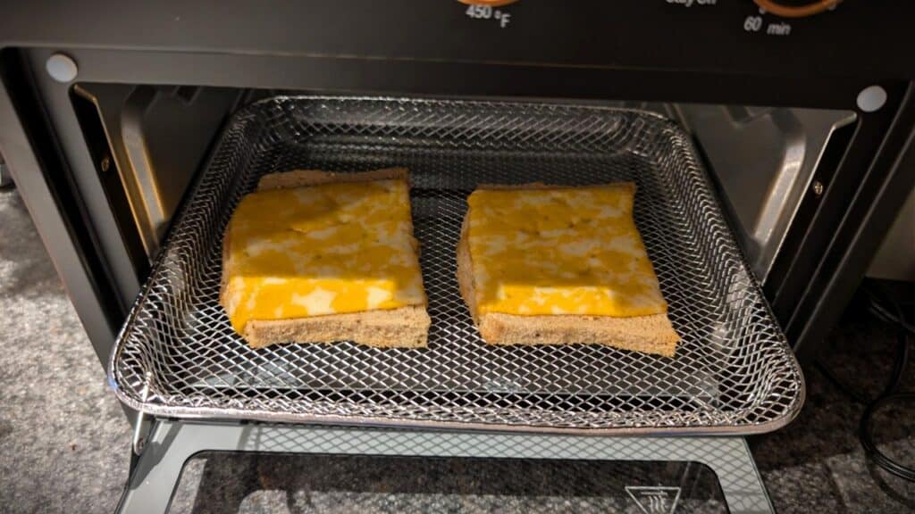Close-up of two toasted cheese sandwiches on a wire rack inside a toaster oven, ready to be enjoyed as a delicious meal or snack.