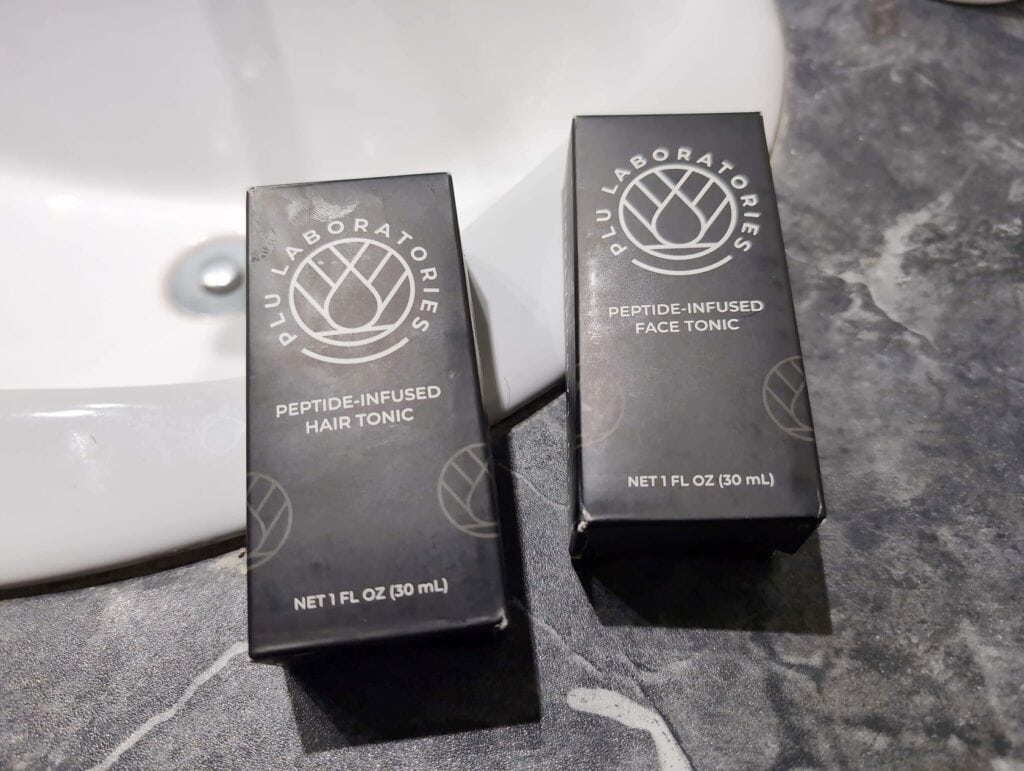 Are Copper Peptides Worth It For Skin And Hair? 5 Black boxes labeled "Peptide-Infused Hair Tonic" from Blue Laboratories.